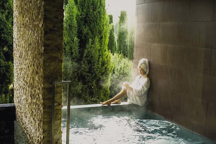 A guest in a robe on the edge of a steaming outdoor mineral pool.