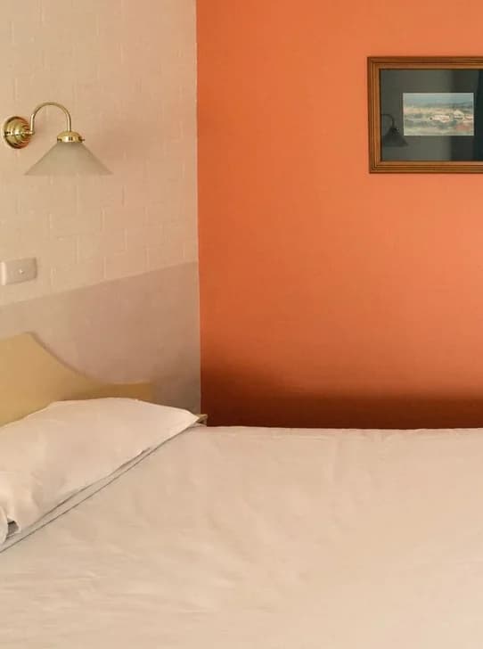 A queen bed against an orange feature wall, with a wall lamp and a framed picture.