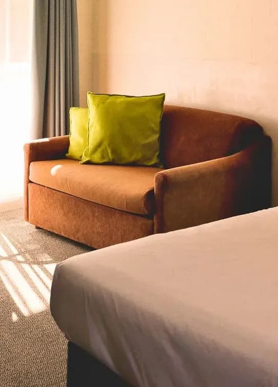 A brown sofa with a green cushion beside the bed in the Twin Room.