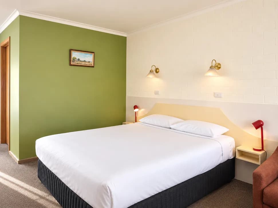 A bed with white linen against a green feature wall in the Twin Room, with brass wall lamps and red bedside lamps.