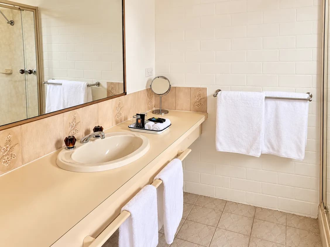 Ensuite vanity with a basin and mirror, white towels on the rails and a tray of toiletries.