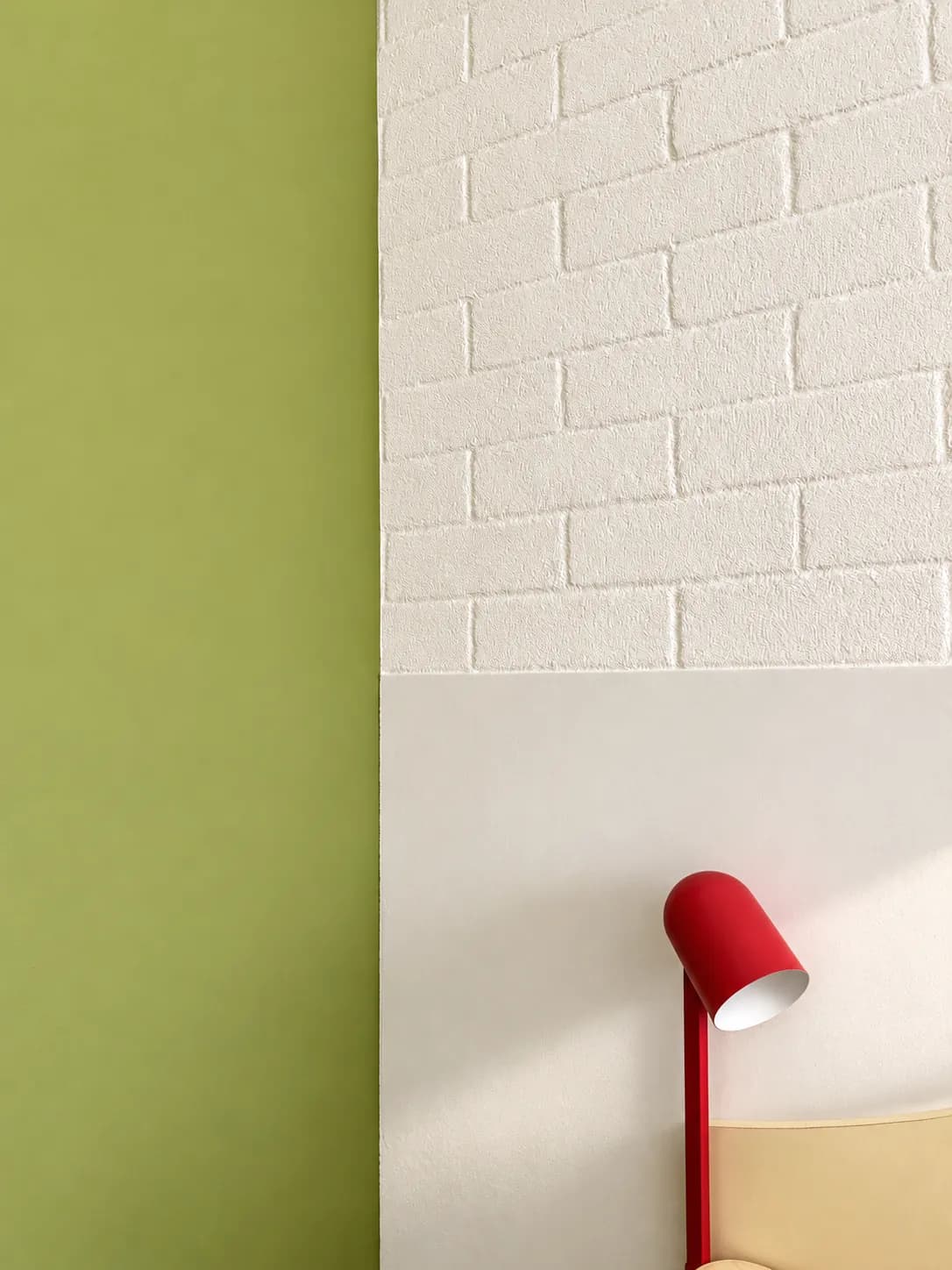 Green feature wall meeting white brick, with a red reading lamp above the bedhead.
