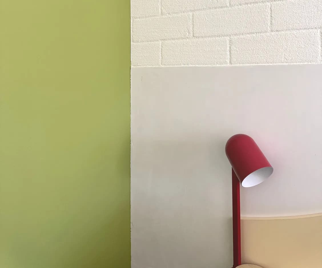 Green feature wall meeting white brick, with a red reading lamp.