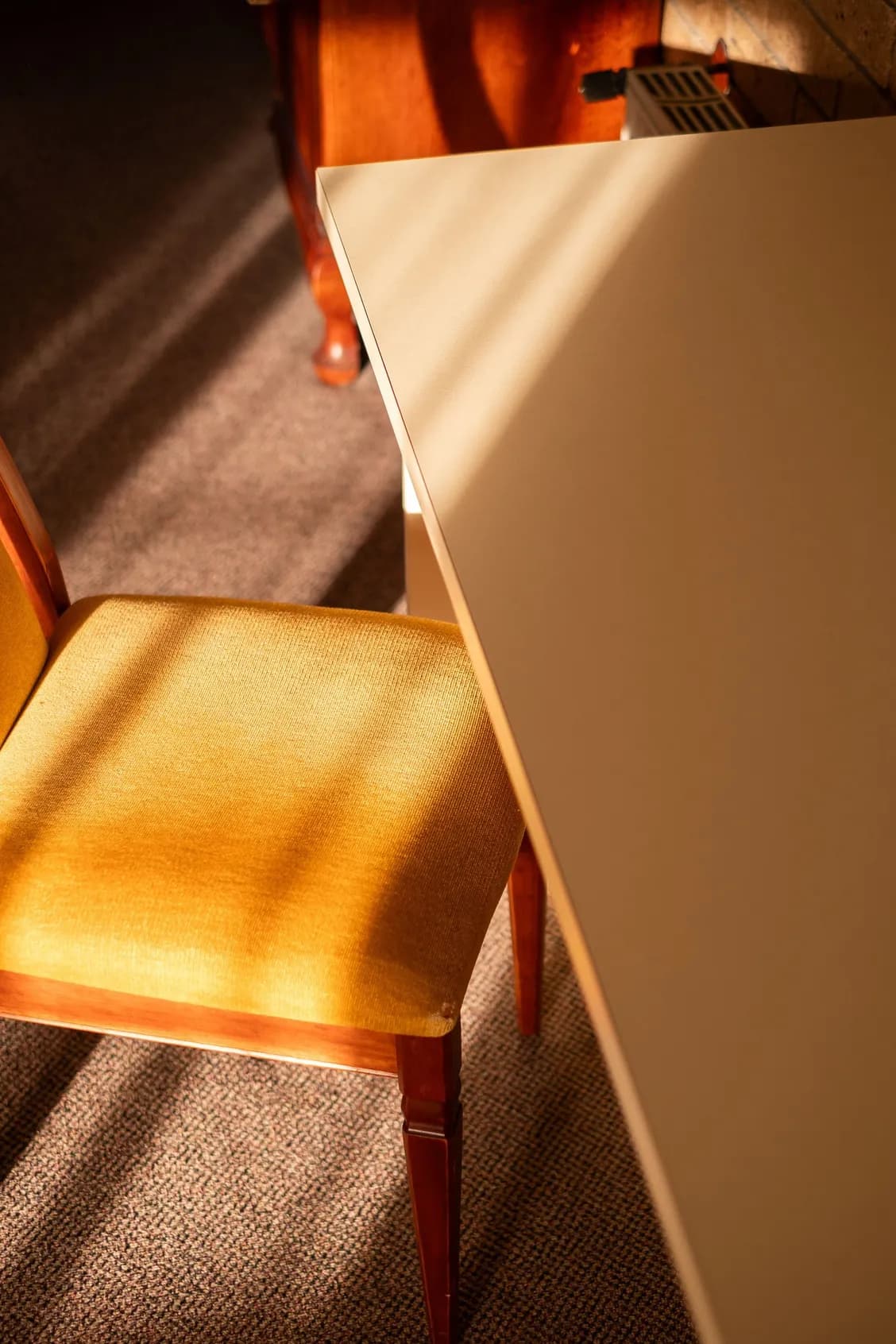 Yellow chair next to a white table, illuminated by sunlight. Brown carpet.