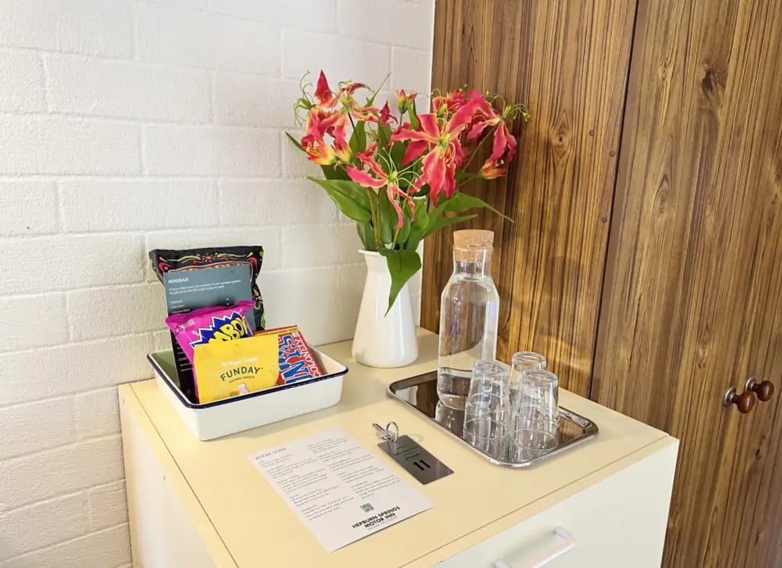 Red lilies in a white jug beside a carafe of water, glasses on a tray, minibar snacks and the room guide.